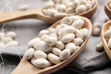 Kumaş arka planında çiğ fasulye olan kaşıklar, yakın plan.