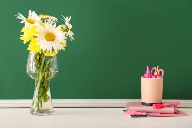 Sınıftaki masada çiçekli vazo ve kırtasiye malzemesi. Öğretmenler Günü kutlaması