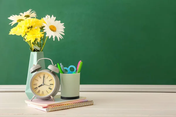 Vase with flowers and stationery on table in classroom. Teacher\'s Day celebration