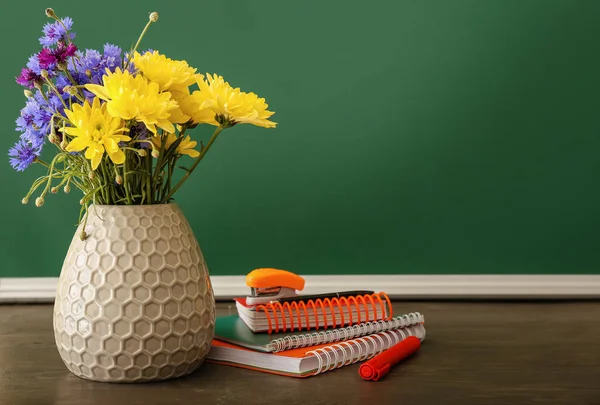 Vase with beautiful flowers and stationery on table in classroom. Teacher\'s Day celebration