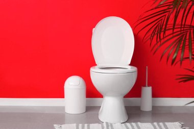 Kırmızı duvarın yanındaki tuvaletin içindeki modern klozet.