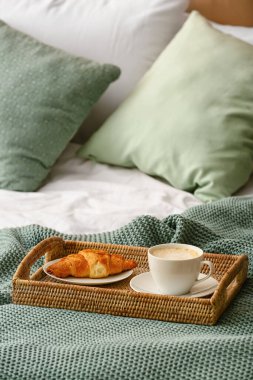 Yatakta bir fincan kahve ve kruvasanla tepsi.