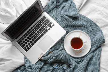 Yatağında aksesuar ve laptop olan bir fincan çay.