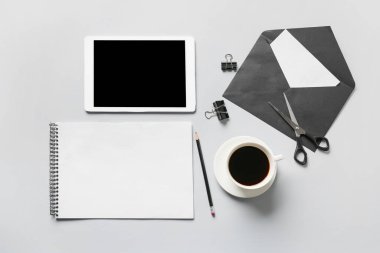 Boş defter, tablet bilgisayar, kırtasiye malzemesi ve gri arkaplanda bir fincan kahve ile kompozisyon