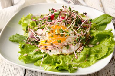 Sebzeli lezzetli salata, sahanda yumurta ve ahşap arka planda mikro yeşil, yakın plan.