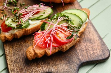 Sebzeli lezzetli kruvasanlar ve renkli ahşap arka planda mikro yeşil, yakın plan.