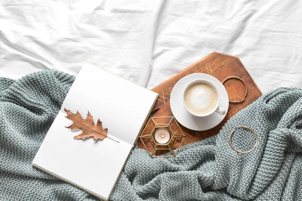 Cup of coffee with book and earrings on bed