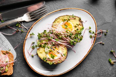 Lezzetli doldurulmuş avokado ve koyu arkaplanda mikro yeşil tabaklar.
