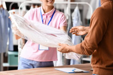 Modern kuru temizlemecideki müşteriye temiz giysiler veren kadın işçi.