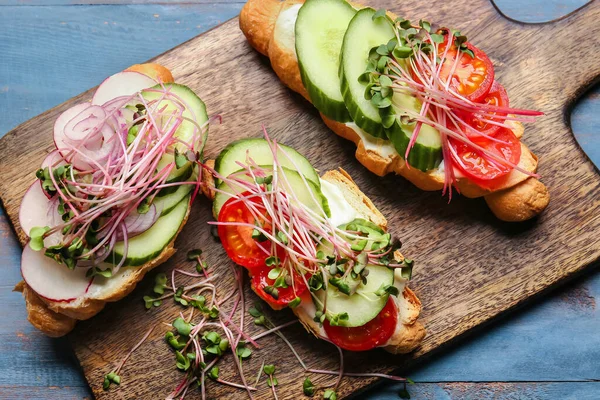 Sebzeli lezzetli kruvasanlar ve renkli ahşap arka planda mikro yeşil, yakın plan.