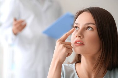 Genç bir kadın göz doktorunun ofisine kontak lens takıyor.
