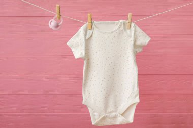 Bebek kıyafetleri ve emzik renkli ahşap arka planda ipte asılı.