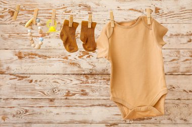 Bebek kıyafetleri, emzik ve ip, tahta arka planda asılı duruyor.