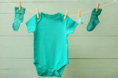 Bebek kıyafetleri ve emzik renkli ahşap arka planda ipte asılı.