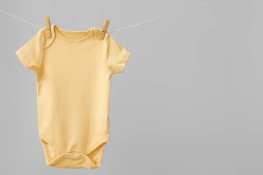 Bebek kıyafetleri gri arka planda ipte asılı.