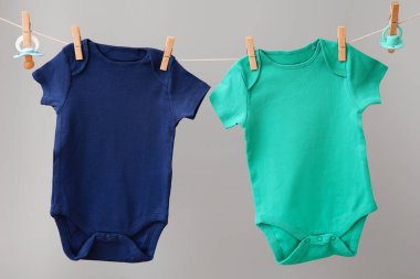 Bebek kıyafetleri ve emzik gri arka planda ipe asılı.