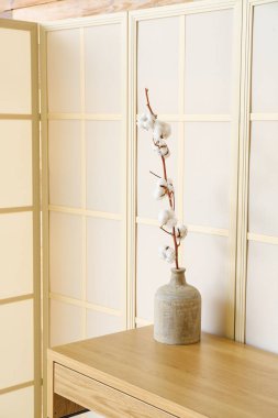 Katlanan ekranın yanındaki masada pamuk çiçekli vazo