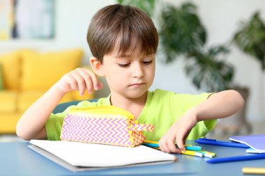 Evdeki kalem kutusuna kırtasiye malzemesi koyan küçük çocuk.