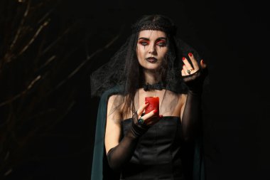 Karanlık arka planda mumu olan genç cadı.