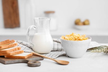 Mutfaktaki masada bir kase lezzetli mısır gevreği, ekmek ve süt.