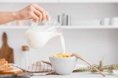 Mutfakta mısır gevreği ve sürahiden kaseye süt döken bir kadın.