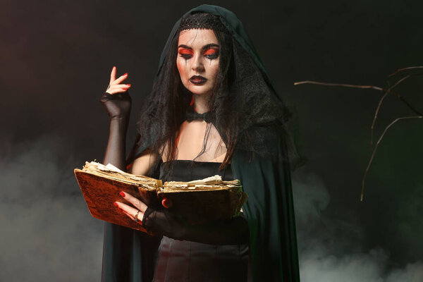 Young witch with spell book on dark background