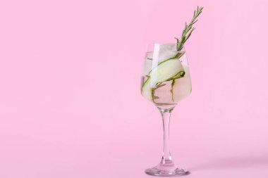 Bir bardak soğuk cin tonik ve arka planda salatalık dilimleri.