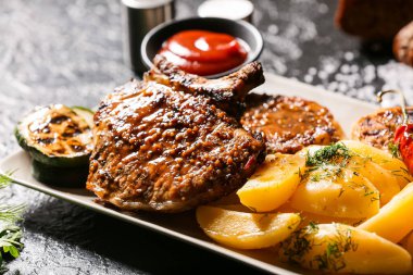 Lezzetli domuz bifteği ve koyu arka planda ızgara sebze tabağı, yakın plan.