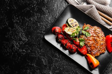 Lezzetli domuz bifteği ve siyah arka planda ızgara sebze tabağı.