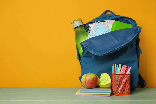 Backpack with stationery and apple on table near color wall