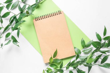 Beyaz arkaplanda boş defter, kağıt ve bitki dalları içeren kompozisyon