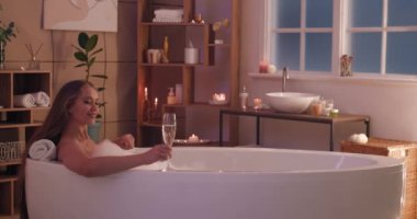 Güzel genç bayan evde banyo yaparken şampanya içiyor.