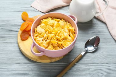 Lezzetli mısır gevreği, kurutulmuş kayısı ve renkli ahşap arka planda bir sürahi süt.