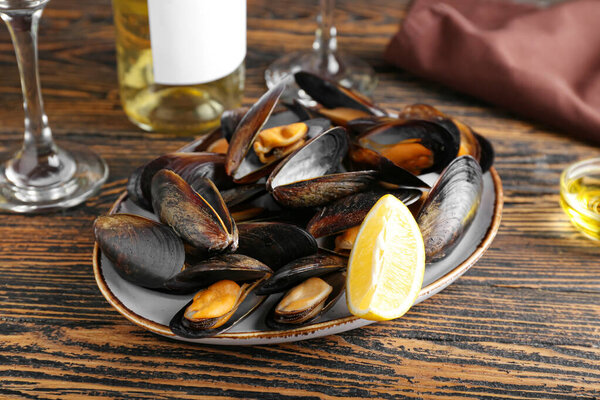 Тарелка вкусных мидий с лимоном на деревянном фоне
