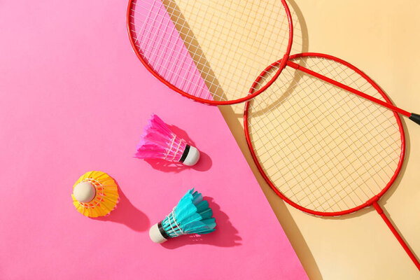 Badminton rackets and shuttlecocks on color background