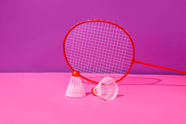 Badminton racket and shuttlecocks on color background