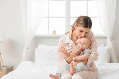 Genç anne yatak odasında tatlı bebeğine su veriyor.