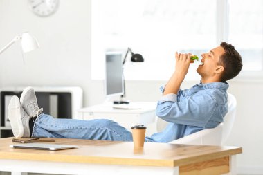 Genç adam ofiste lezzetli sandviçler yiyor.