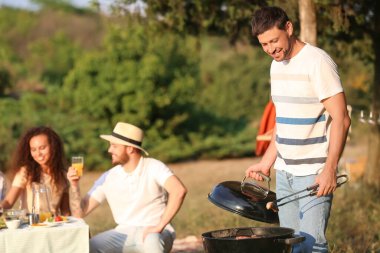 Genç adam dışarıda ızgarada yemek pişiriyor.
