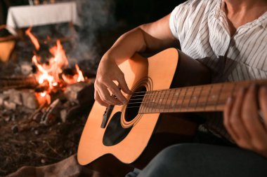 Yaz akşamı barbekü partisinde ateşin yanında gitar çalan olgun bir kadın.