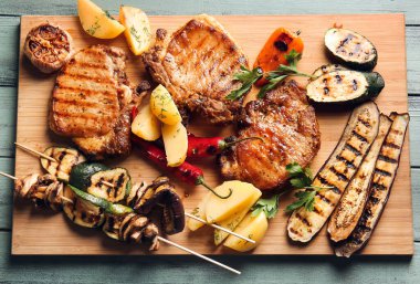 Lezzetli domuz bifteği ve rengarenk ahşap arka planda ızgara sebze.