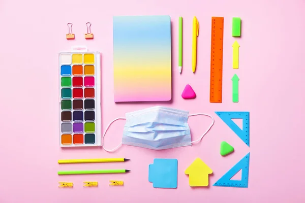 Stationery supplies with medical mask on color background