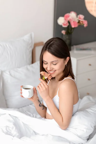 在卧室里喝一杯咖啡和鲜花的年轻女人 — 图库照片