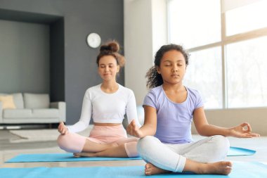 Annesiyle birlikte evde yoga yapan Afro-Amerikalı küçük bir kız.