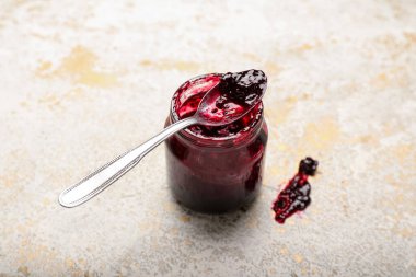 Kavanozda siyah frenk üzümü reçeli ve hafif arka planda kaşık.