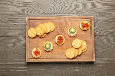 Süzme peynirli lezzetli krakerler ve gri ahşap masada jalapeno biber reçeli.