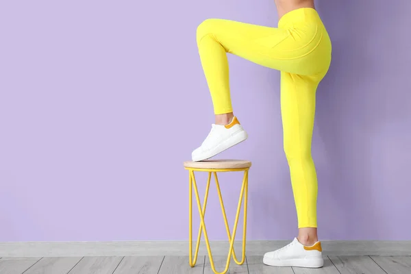 Sporty young woman with chair near color wall