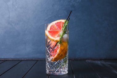 Bir bardak soğuk cin tonik ve koyu ahşap arka planda greyfurt dilimleri.