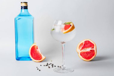 Bir bardak soğuk cin tonik ve arka planda greyfurt dilimleri.