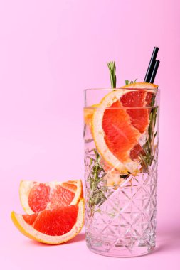 Bir bardak soğuk cin tonik ve arka planda greyfurt dilimleri.